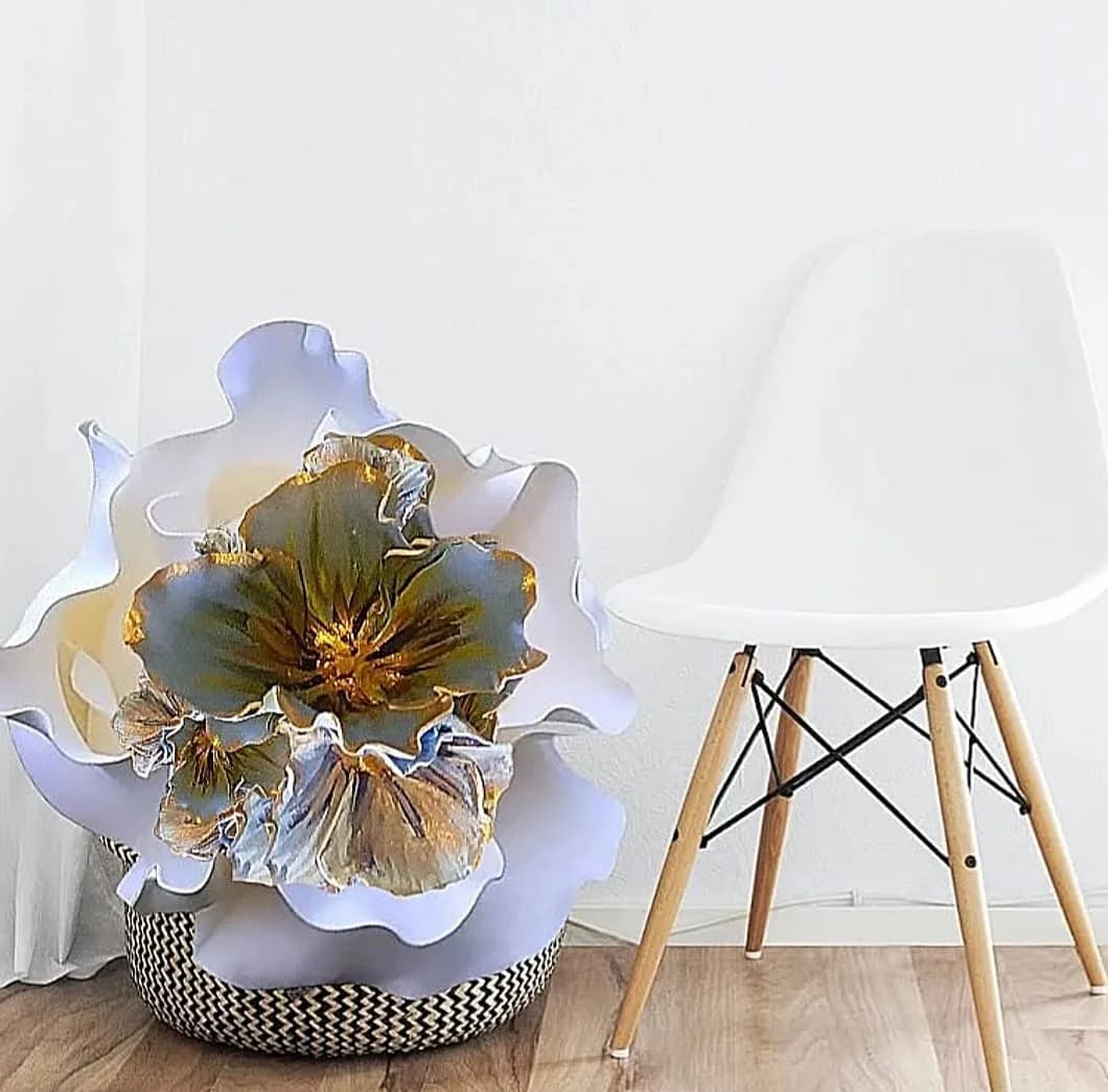 Grande fiore artistico bianco e oro in un cesto, accanto a una sedia di design