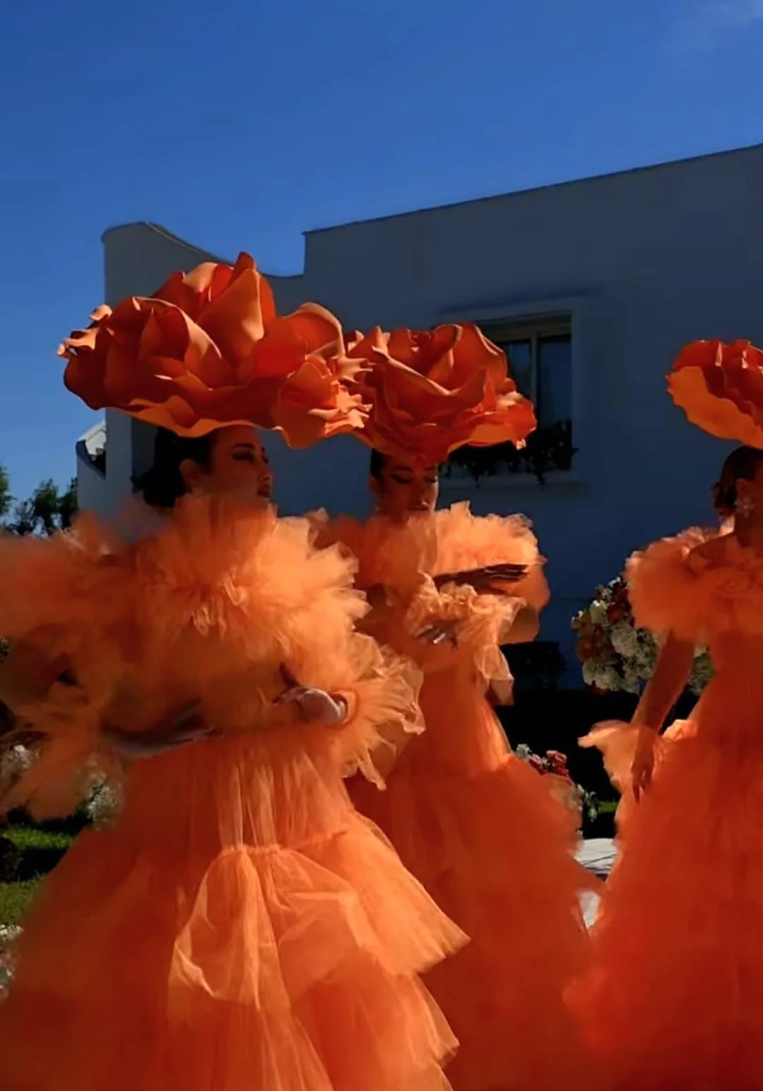 Tre modelle con testali a forma di grande rosa arancione e abiti in tulle arancio