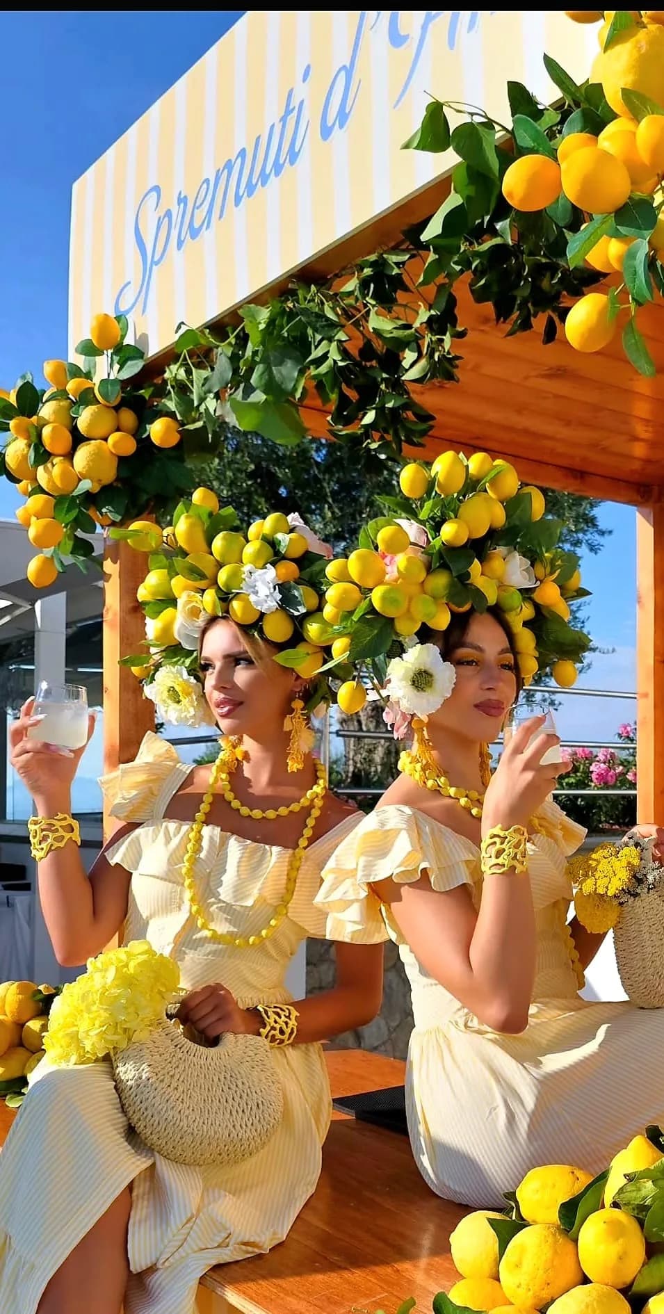 Due modelle con testali di limoni e fiori bianchi a un banco di limonata